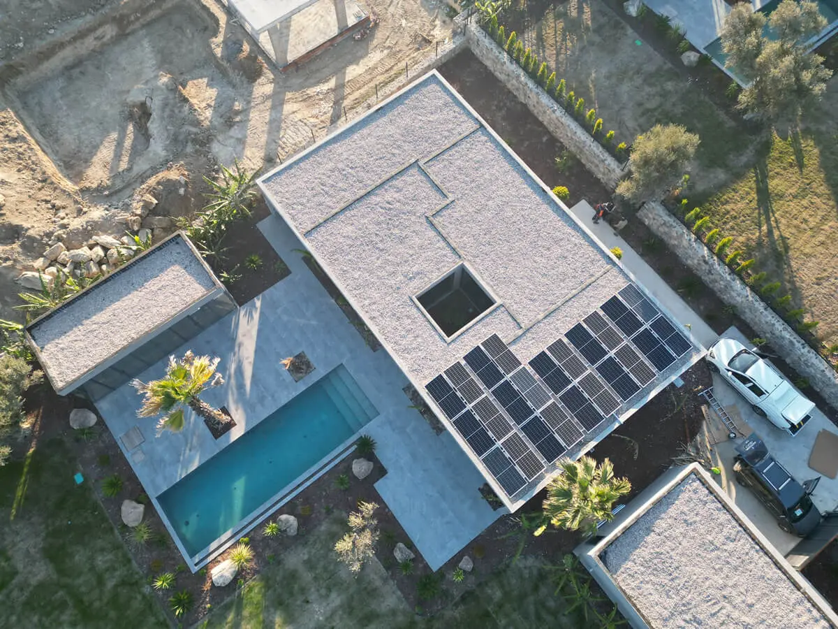 A row of solar panels on the flat roof of a single-story house with a pool; aerial view